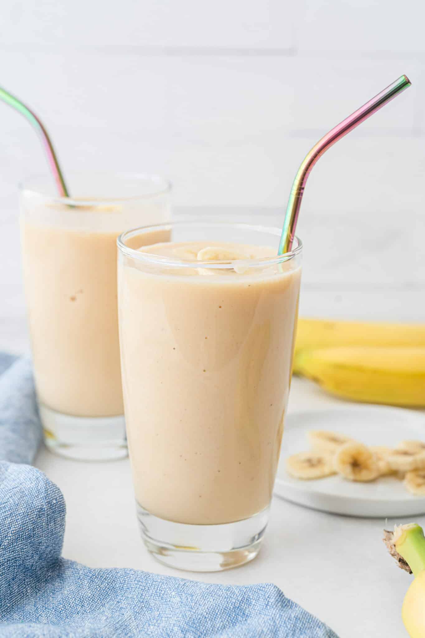 Banana peach smoothie in two glasses with iridescent straws.