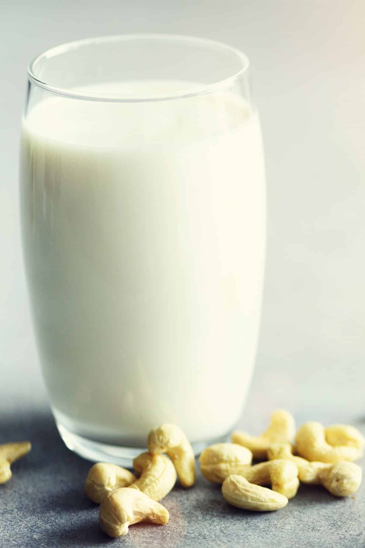 Glass of cashew milk with cashews on white table.