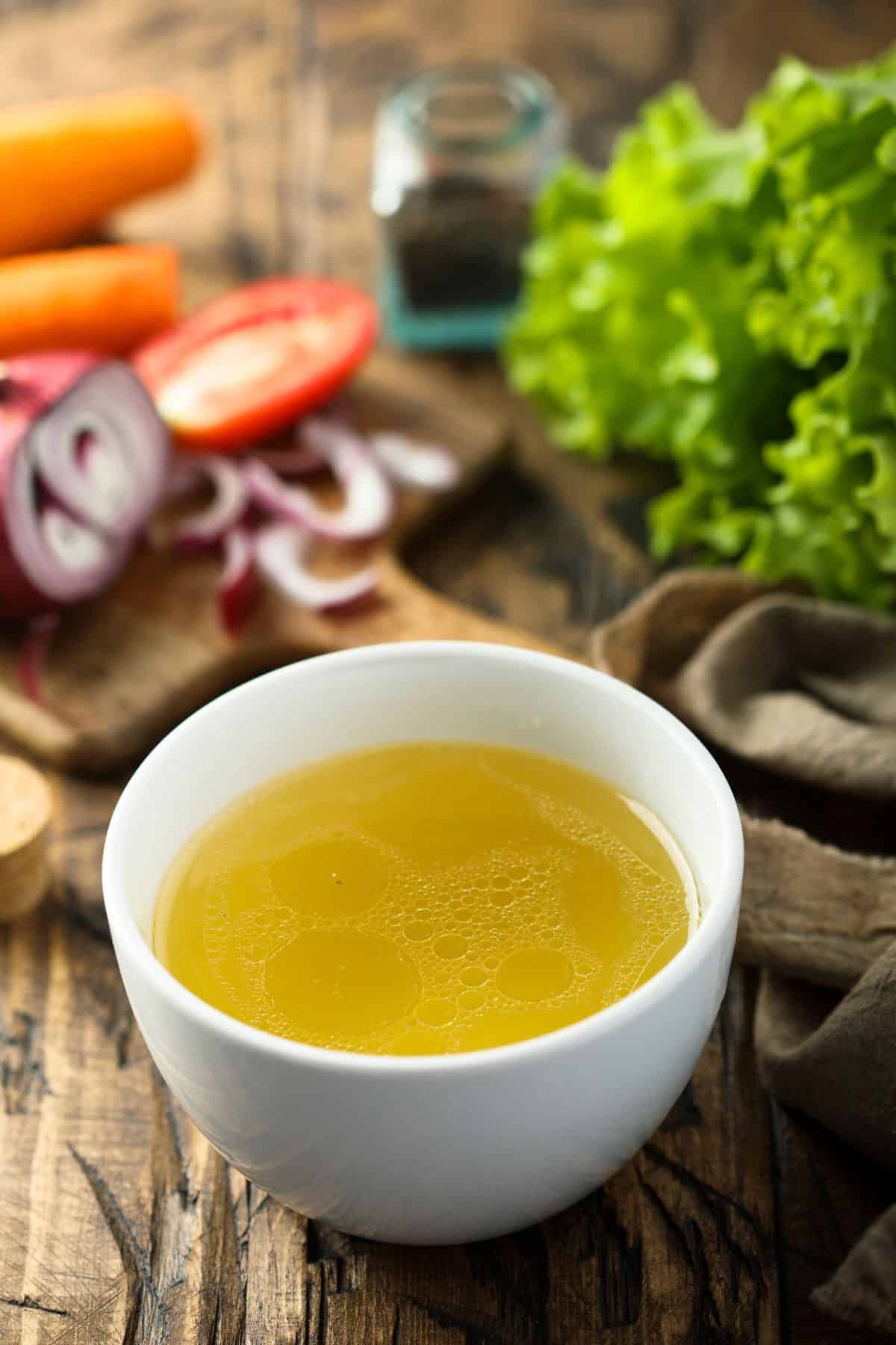 Bowl of chicken broth with veggies on table.