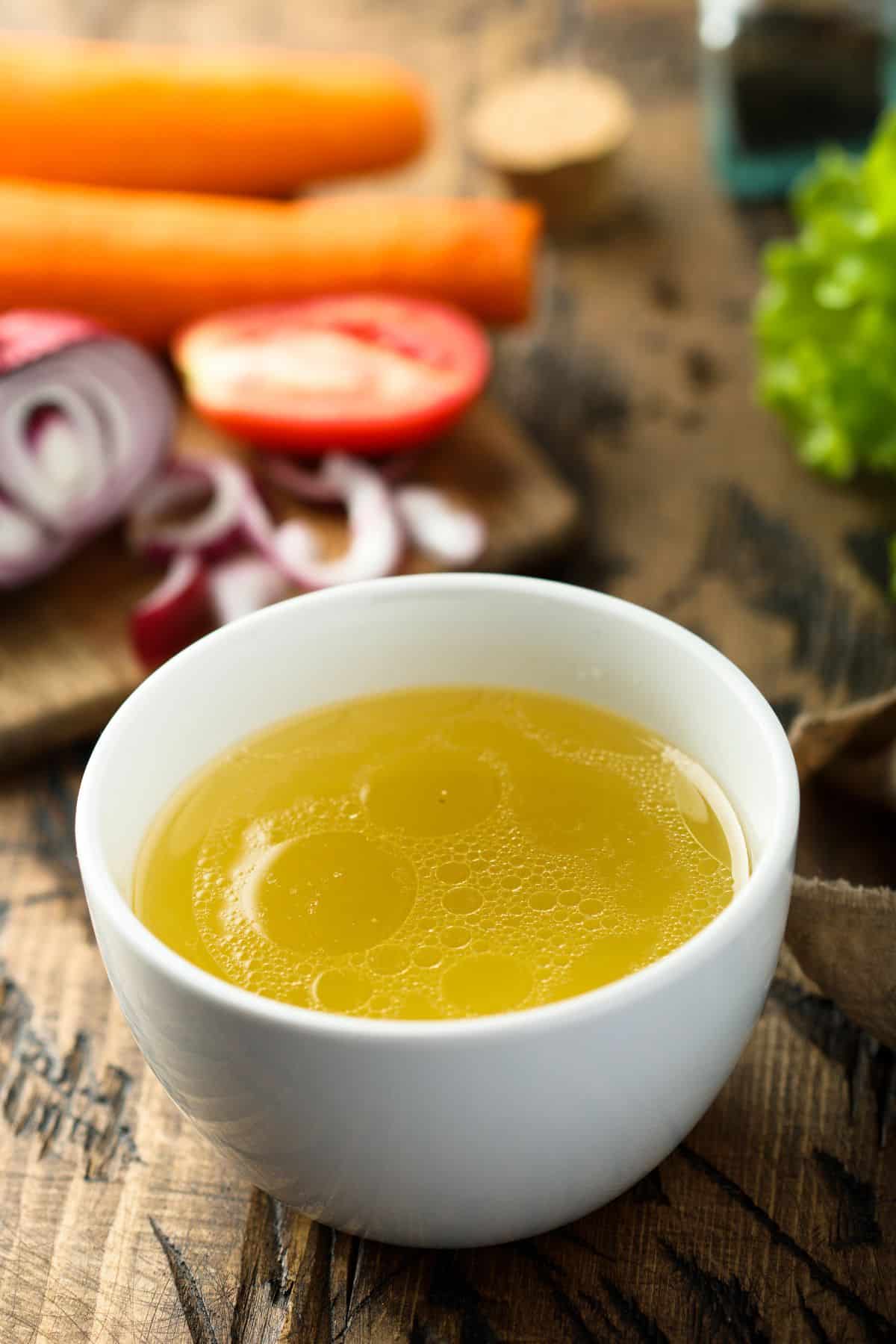 Bowl of chicken stock with cutting board and vegetables.