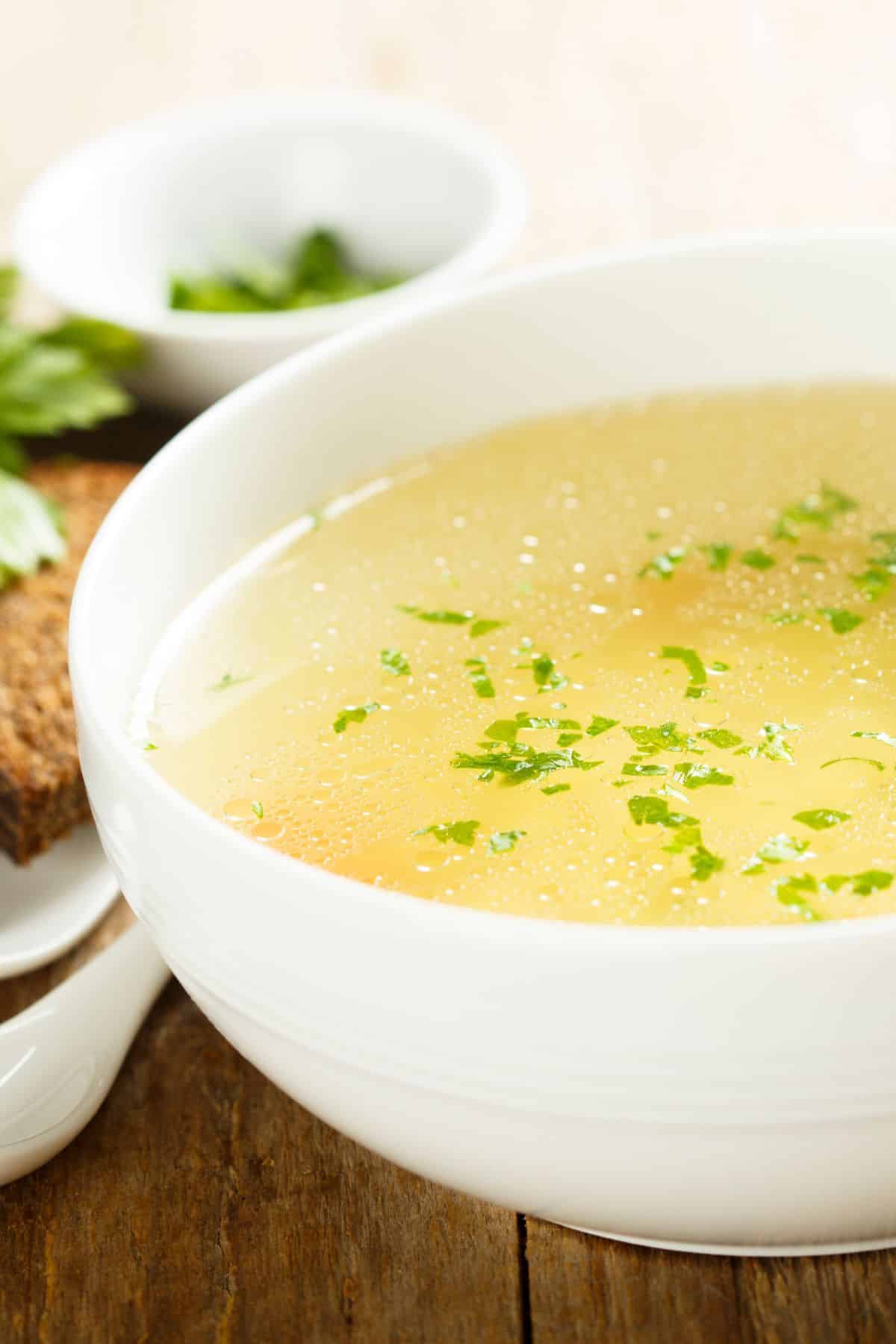 Bowl of chicken broth and sliced bread with herbs.