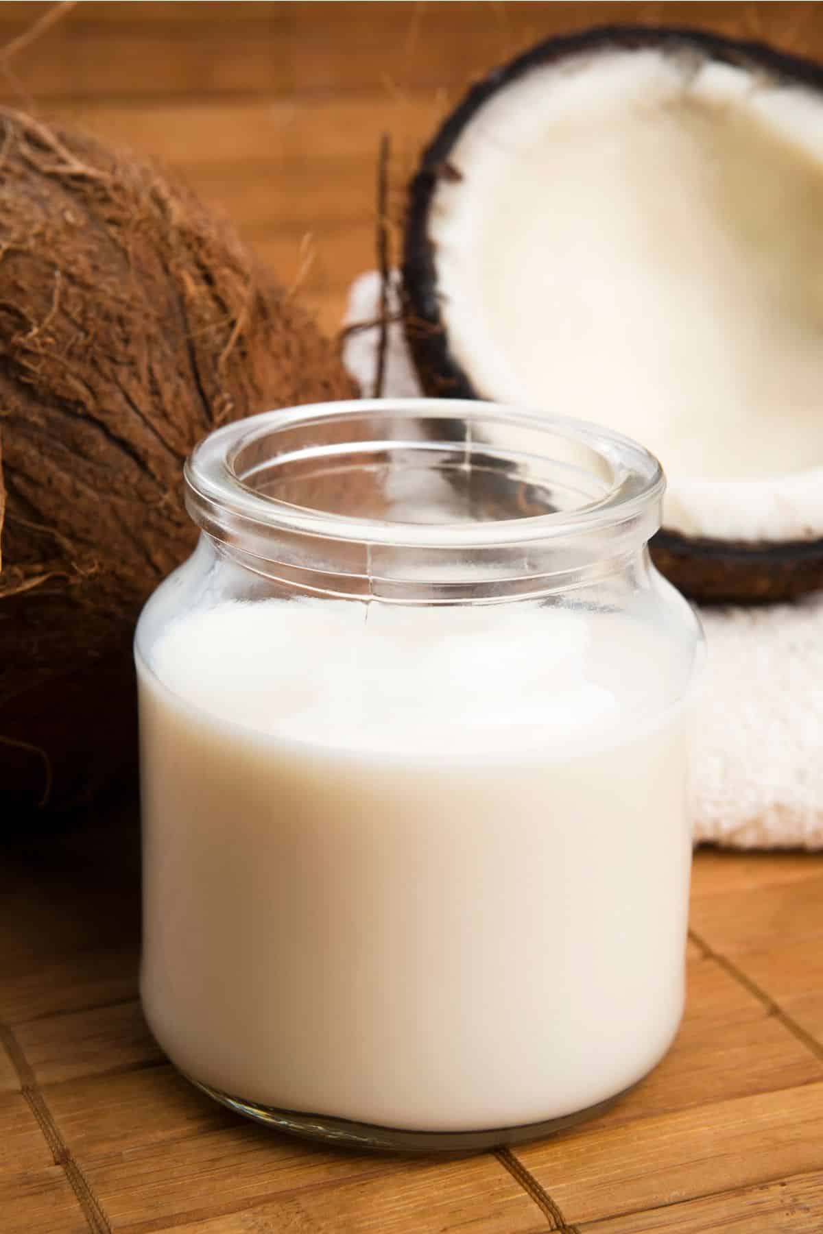 Jar of coconut milk with sliced coconuts.