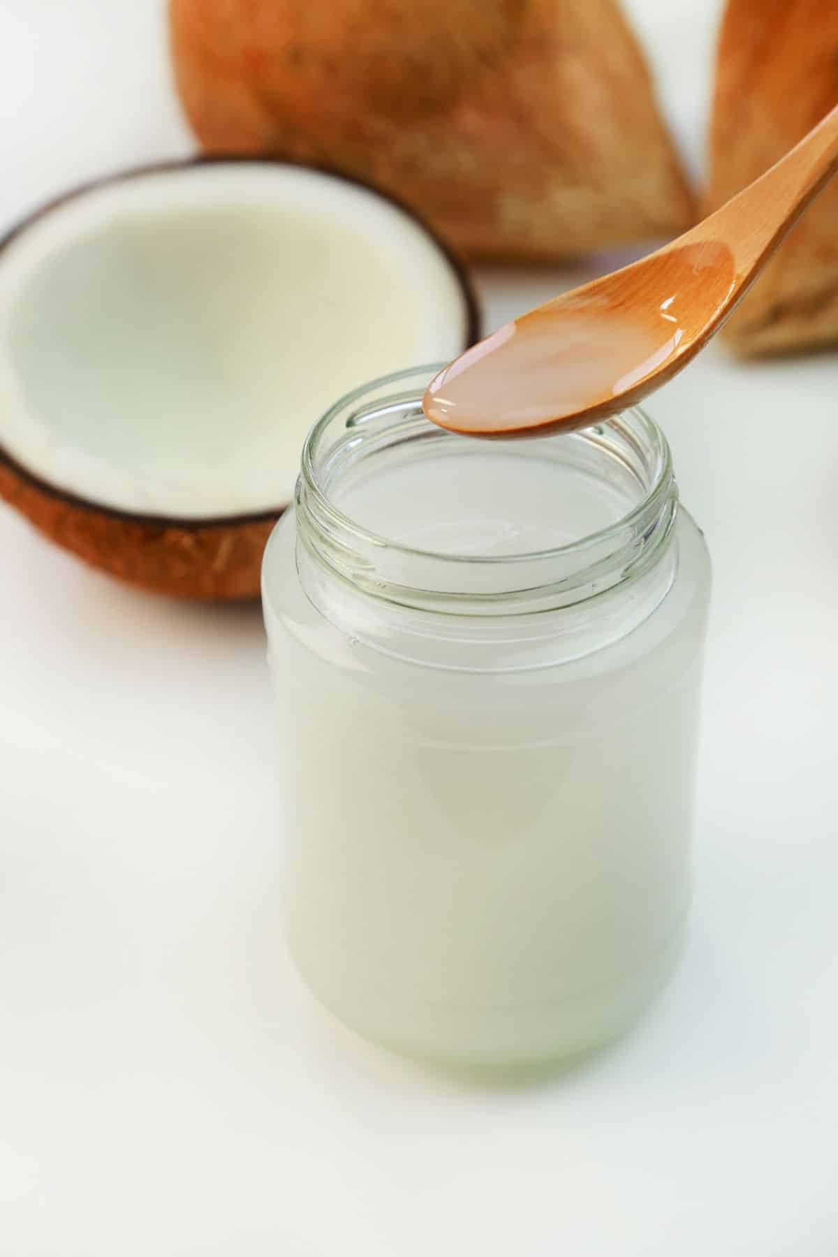 Spoon and jar of coconut oil next to coconut.