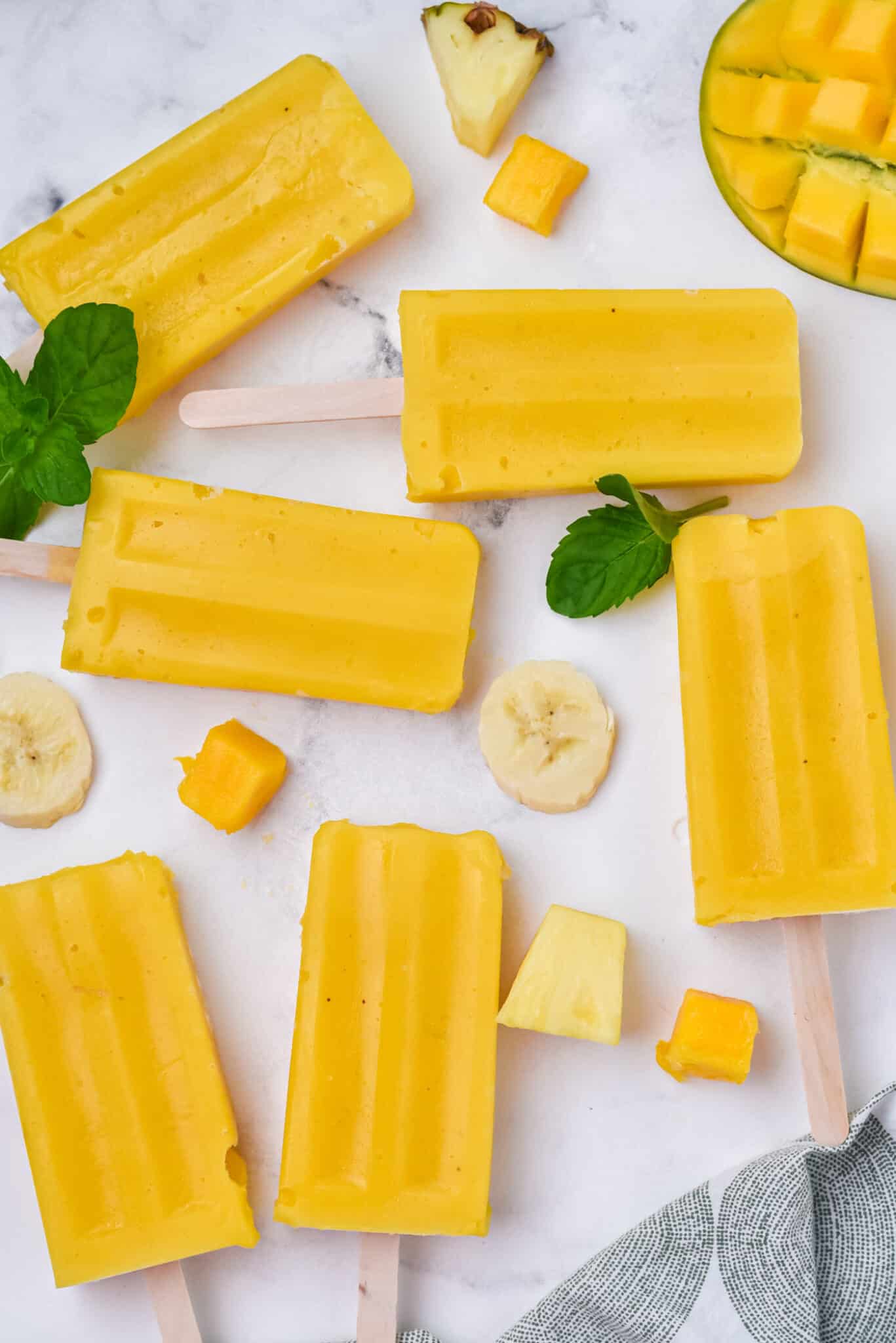 Mango popsicles set out on a white marble surface.