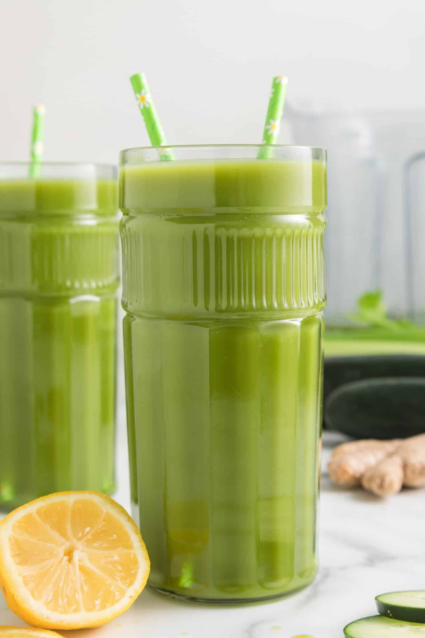 Two tall glasses of lemon ginger green juice, each with two straws.