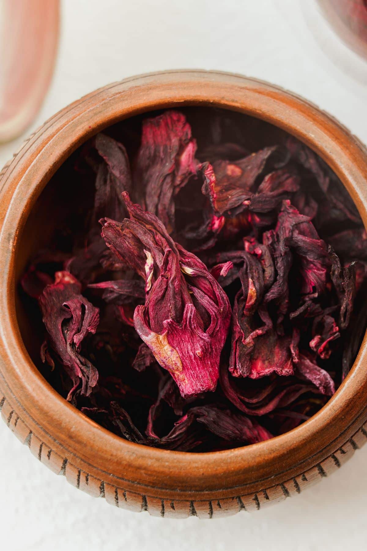 Wooden bowl filled with red hibiscus flower petals.