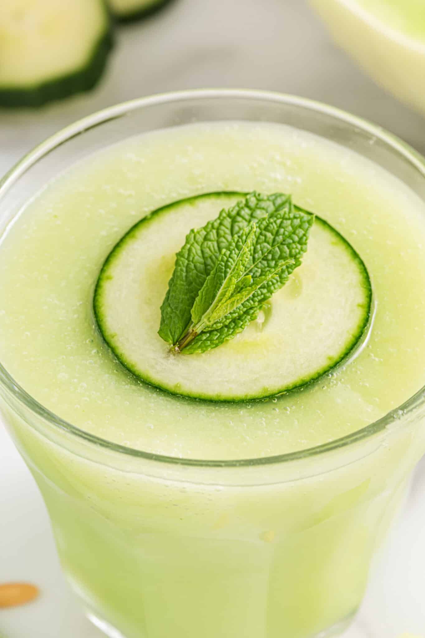Closeup of a cucumber slice and mint leaf floating on a glass of Honeydew Smoothie.