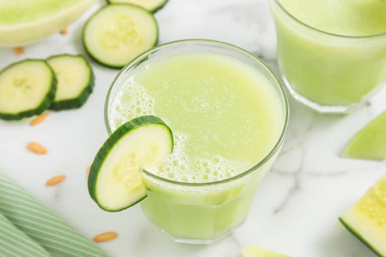 A small glass filled with Honeydew Cucumber Smoothie with a cucumber slice on the rim.