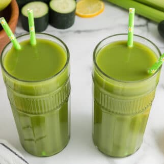 Two tall glasses of lemon ginger green juice, each with two straws.