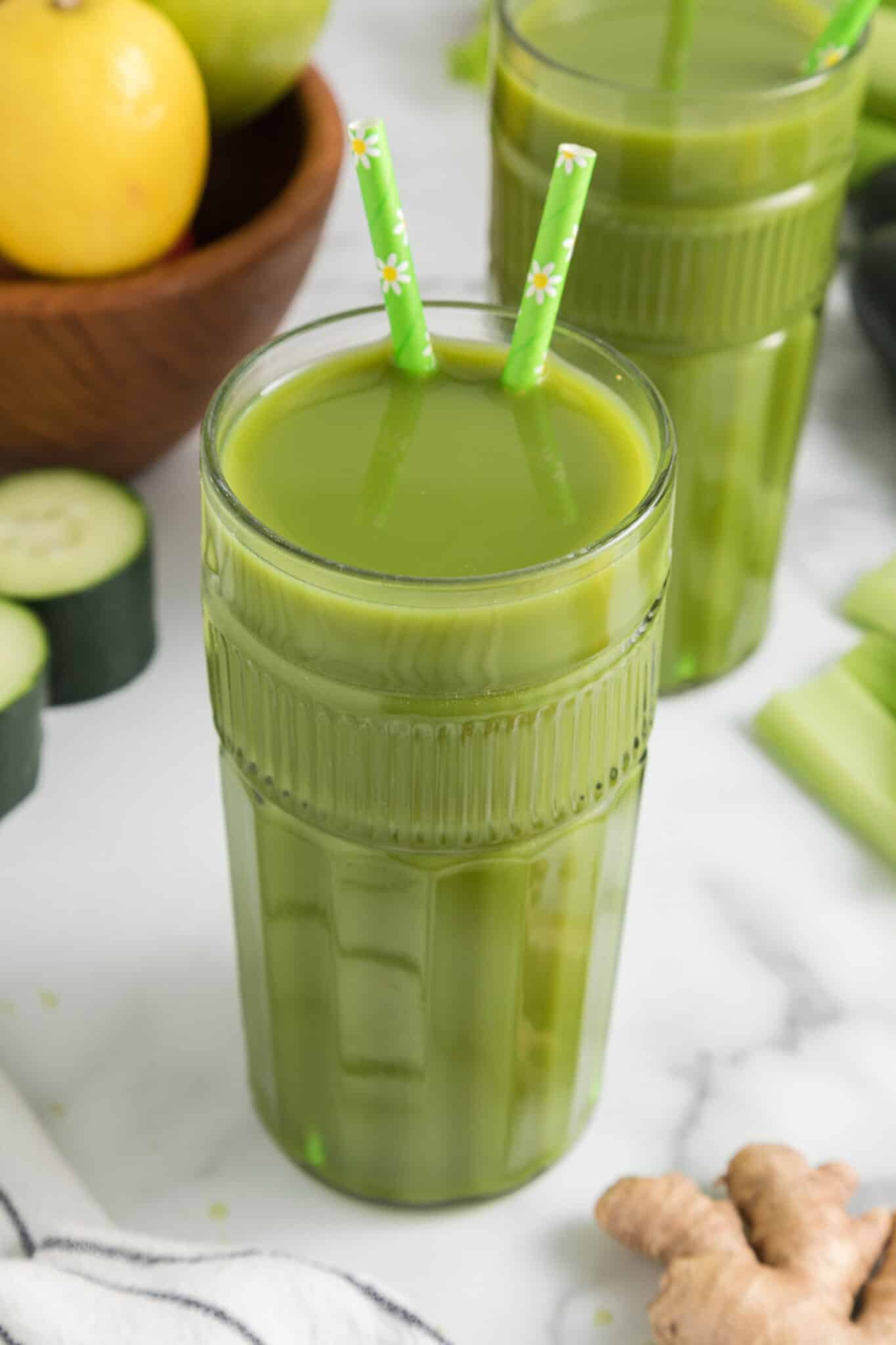 A tall glass of lemon ginger green juice with two straws.