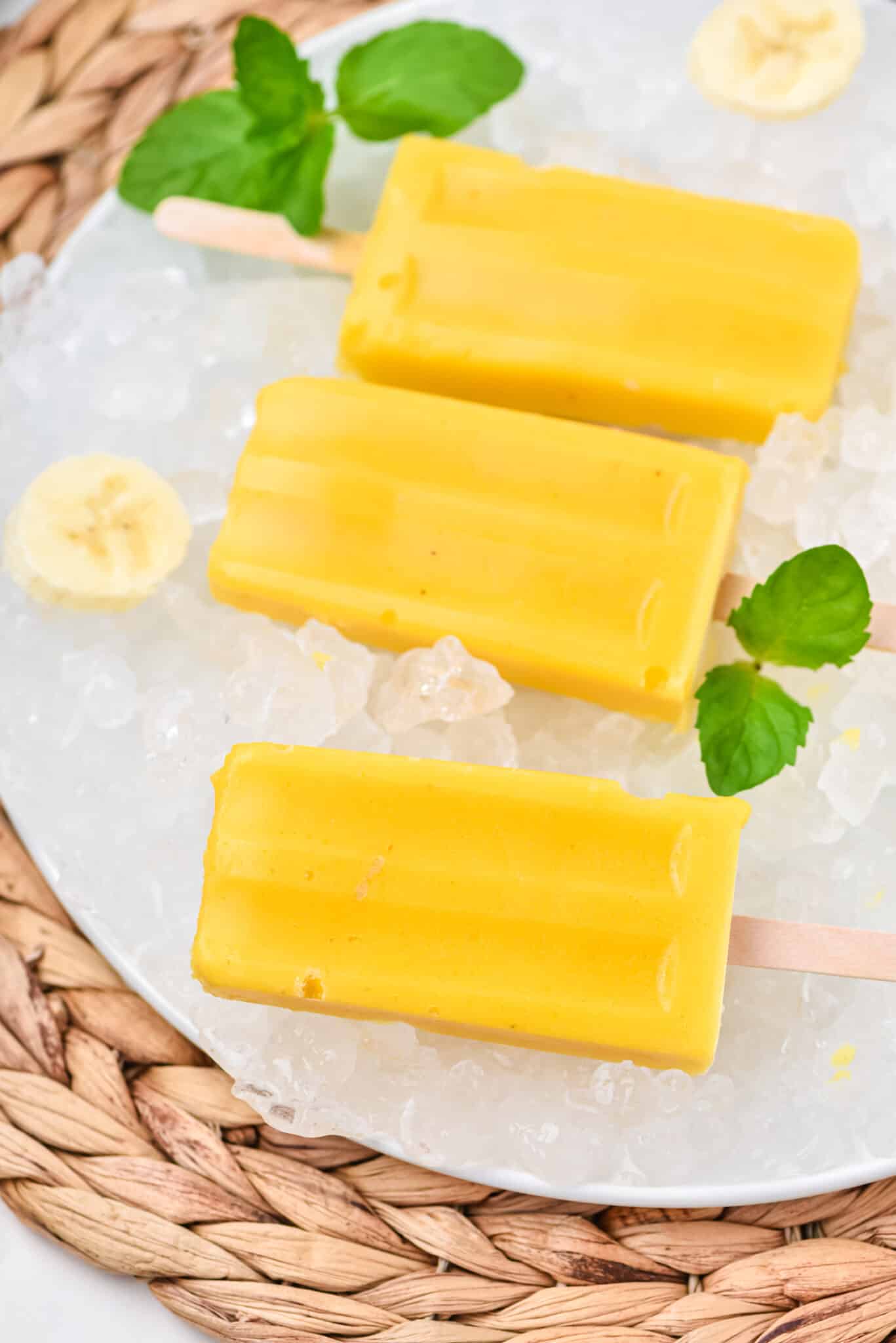 Mango popsicles set out on a plate of ice cubes.