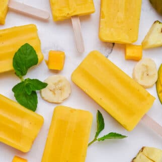 Mango popsicles set out on a white marble surface.