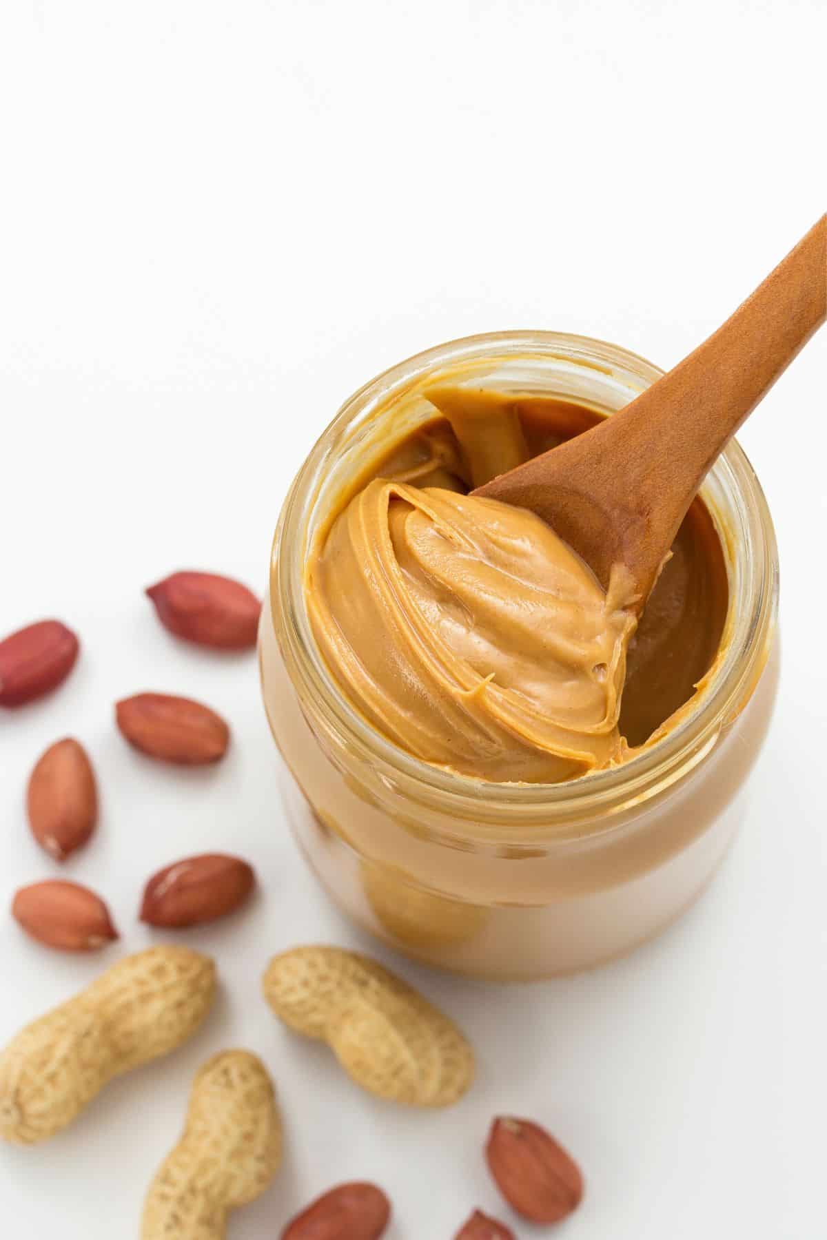 Jar of peanut butter beside peanuts.