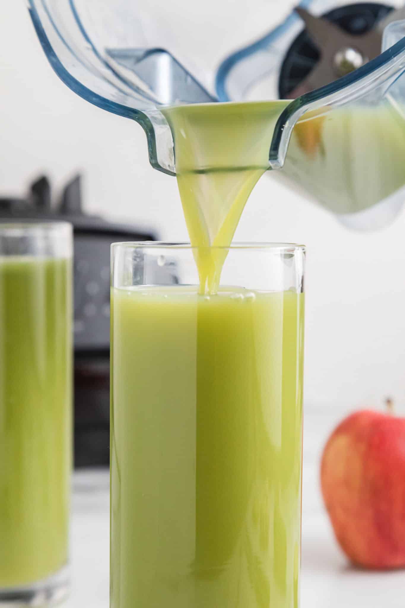 Cucumber celery juice being poured into a glass from the jar of a blender.