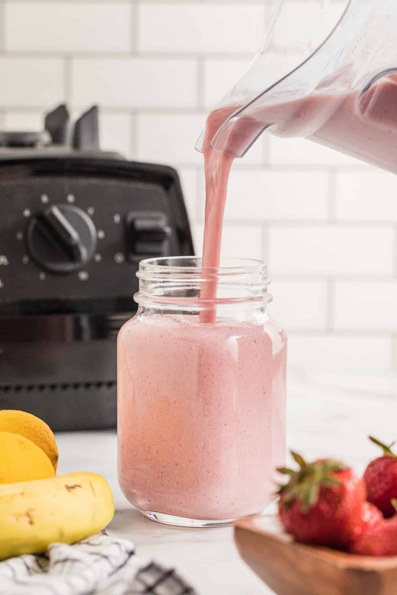A Strawberry Cheesecake Smoothie being poured into a mason jar from a blender.