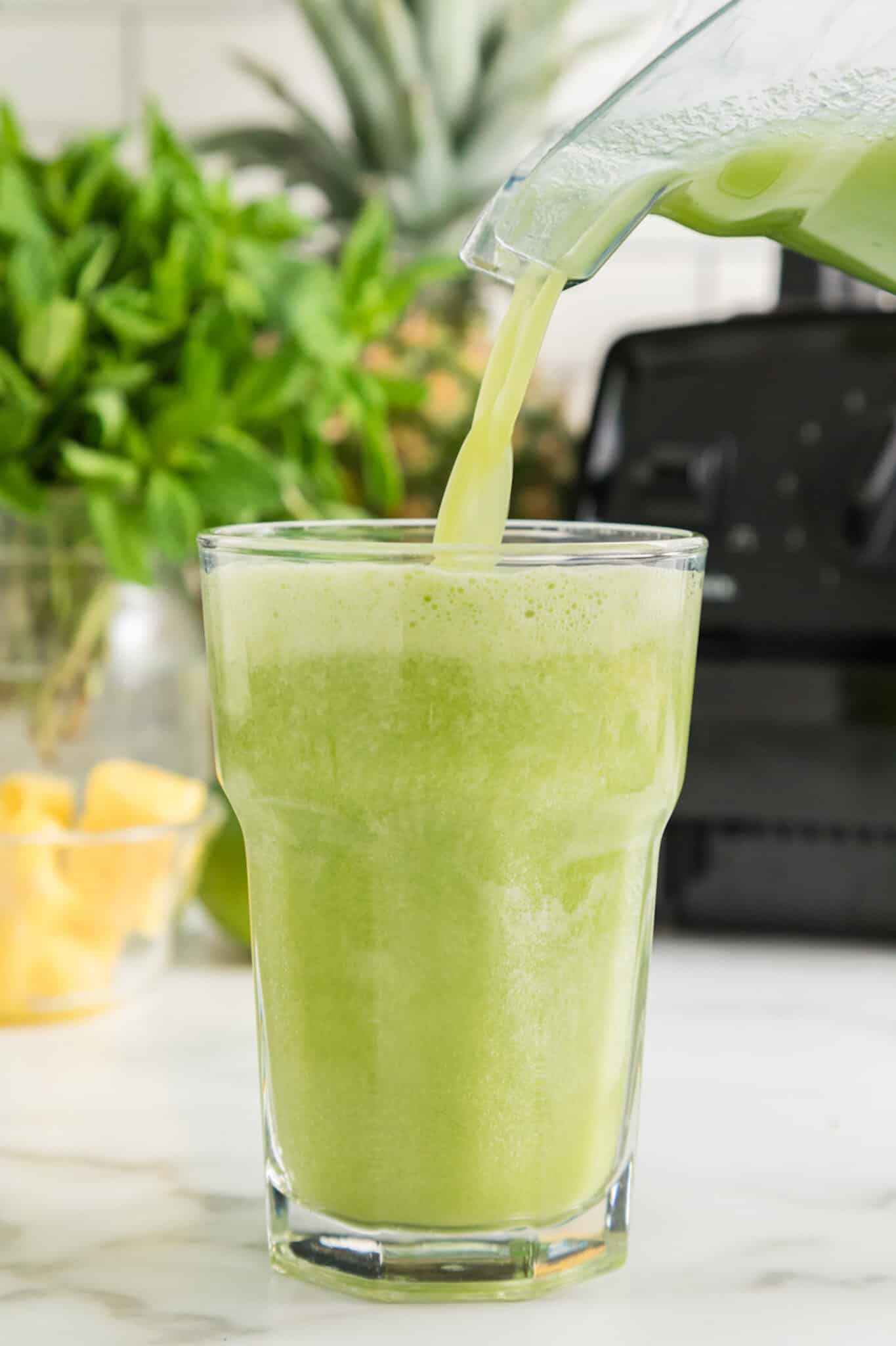 A blender pouring pineapple cucumber smoothie into a glass.