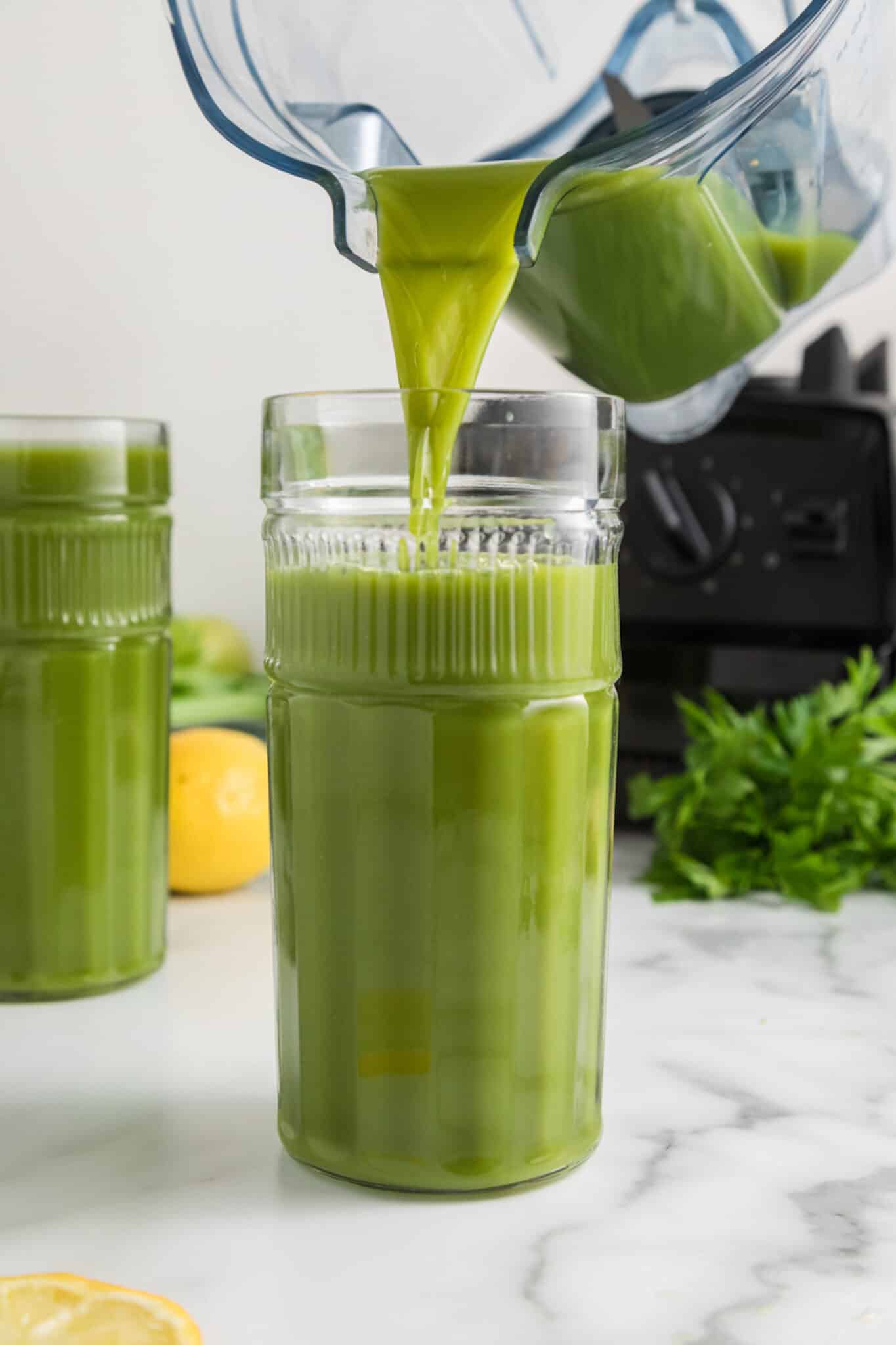 pouring green juice recipe from blender into a tall glass.