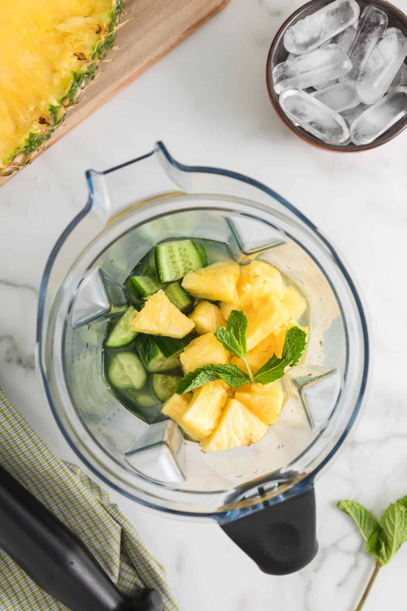 A blender Jar filled with ingredients to make a pineapple cucumber smoothie.