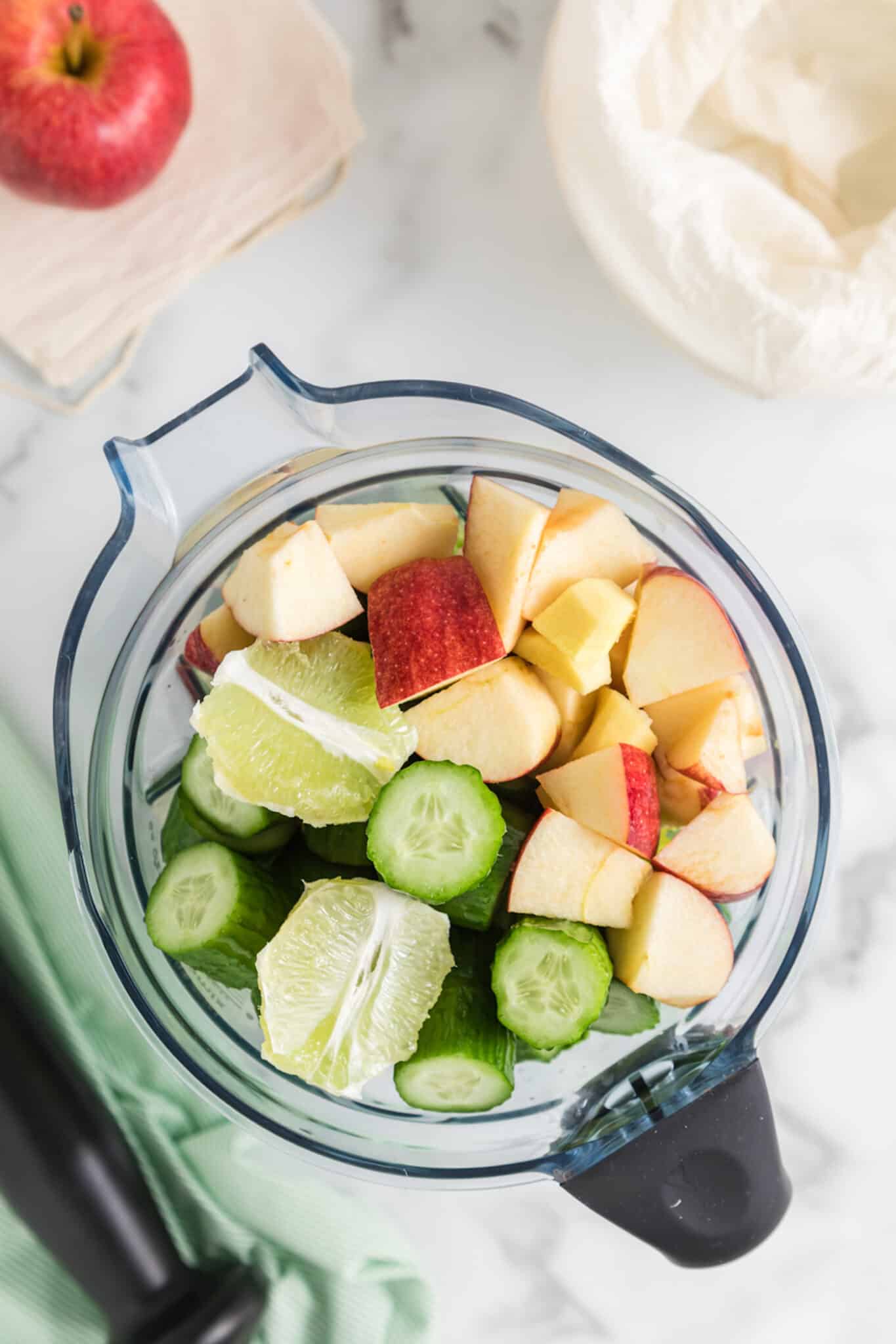 Diced apples, cucumbers, and limes in the jar of a blender.