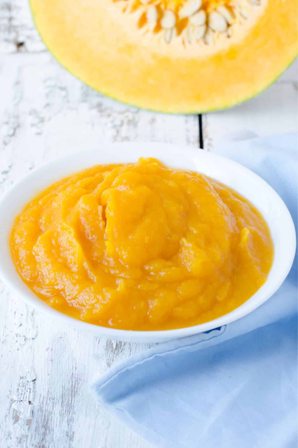 Bowl of pumpkin puree beside sliced pumpkin.