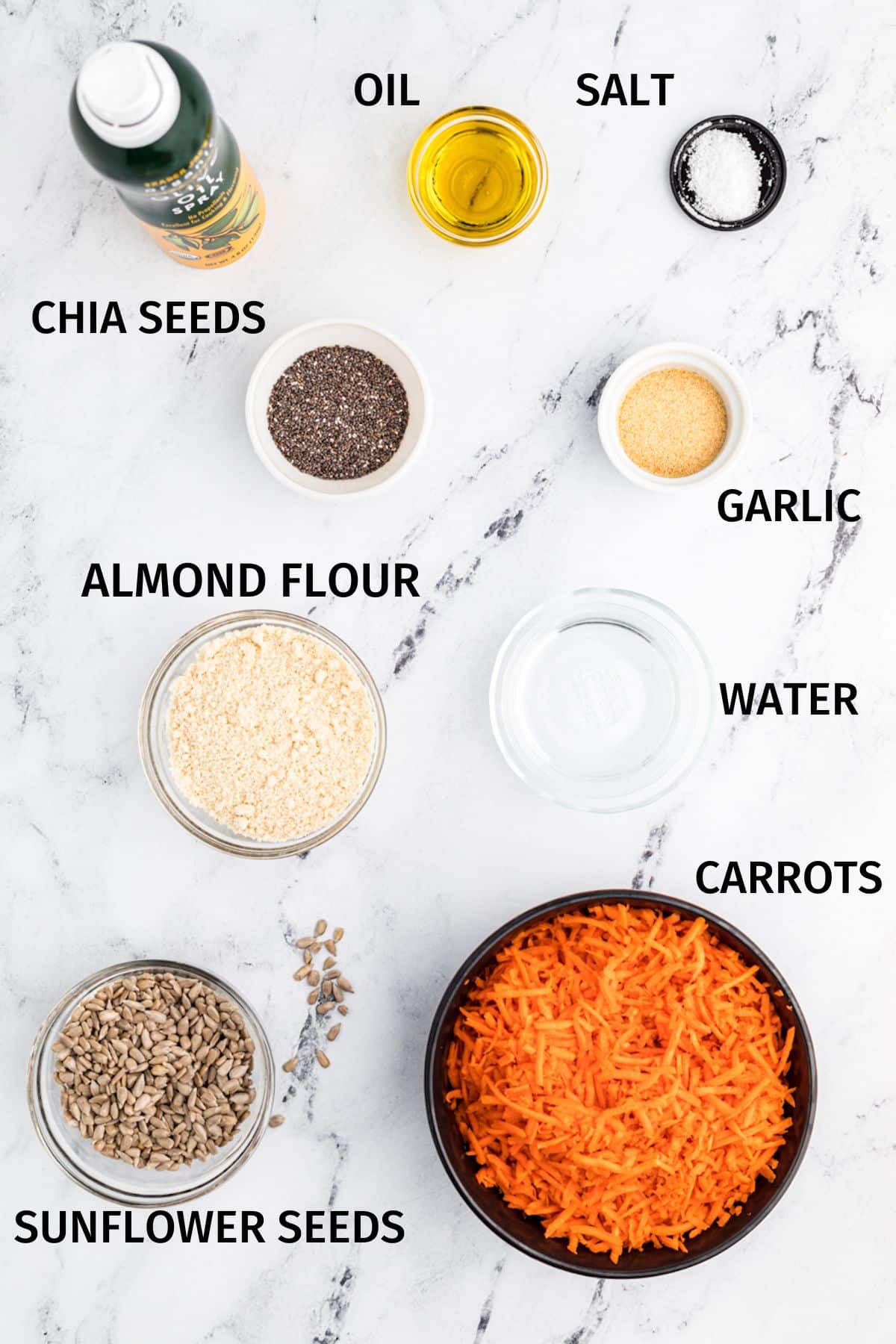 Ingredients to make carrot crackers in small bowls on a white surface.
