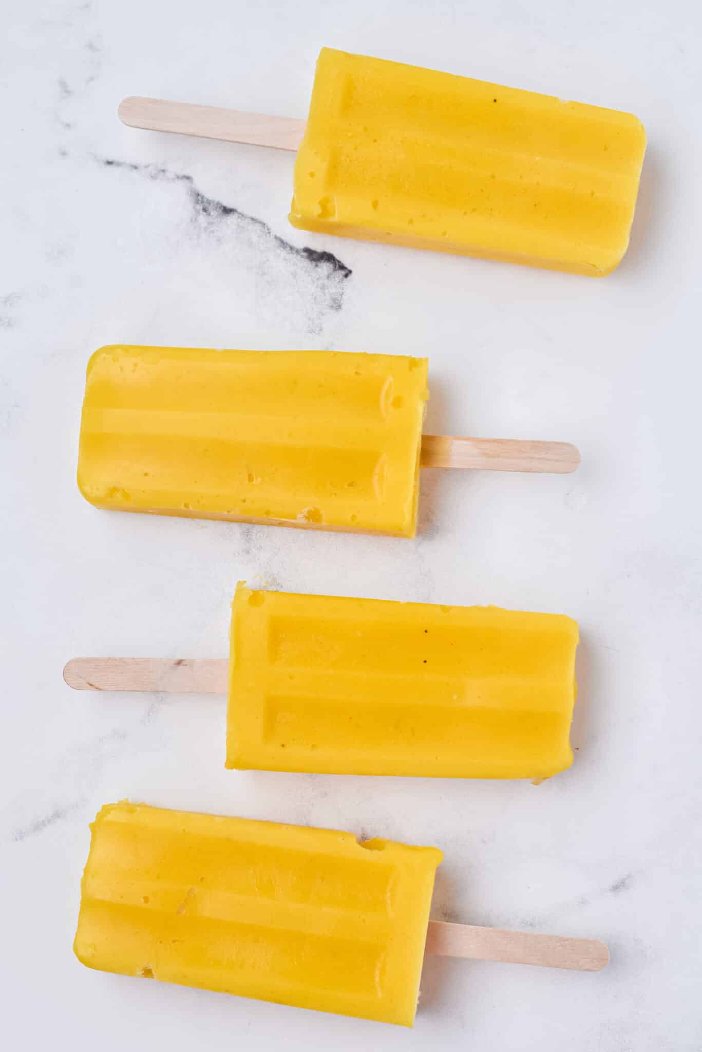 four mango popsicles on a marble table.