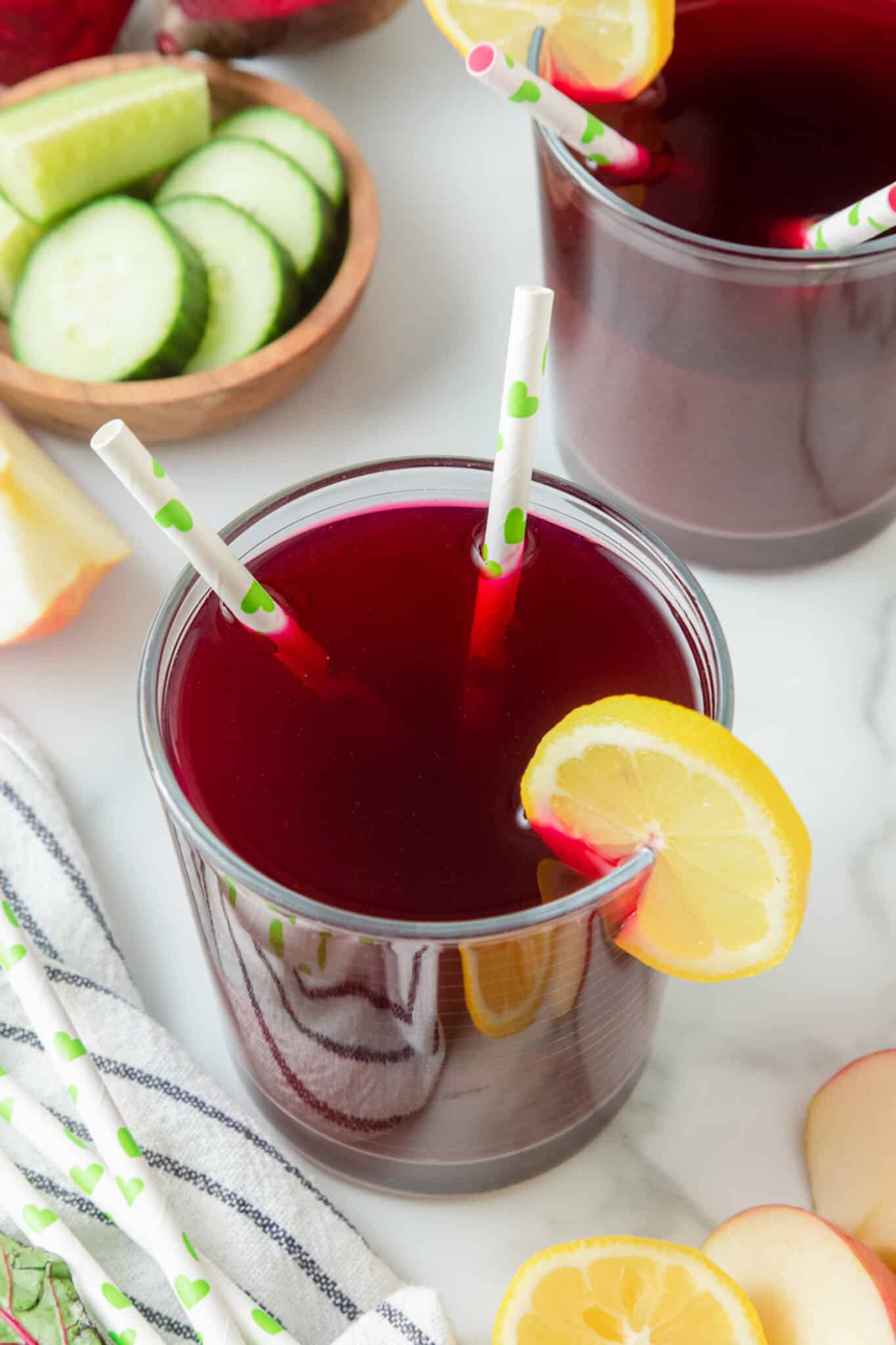 A glass of beet juice with two straws and a lemon slice.