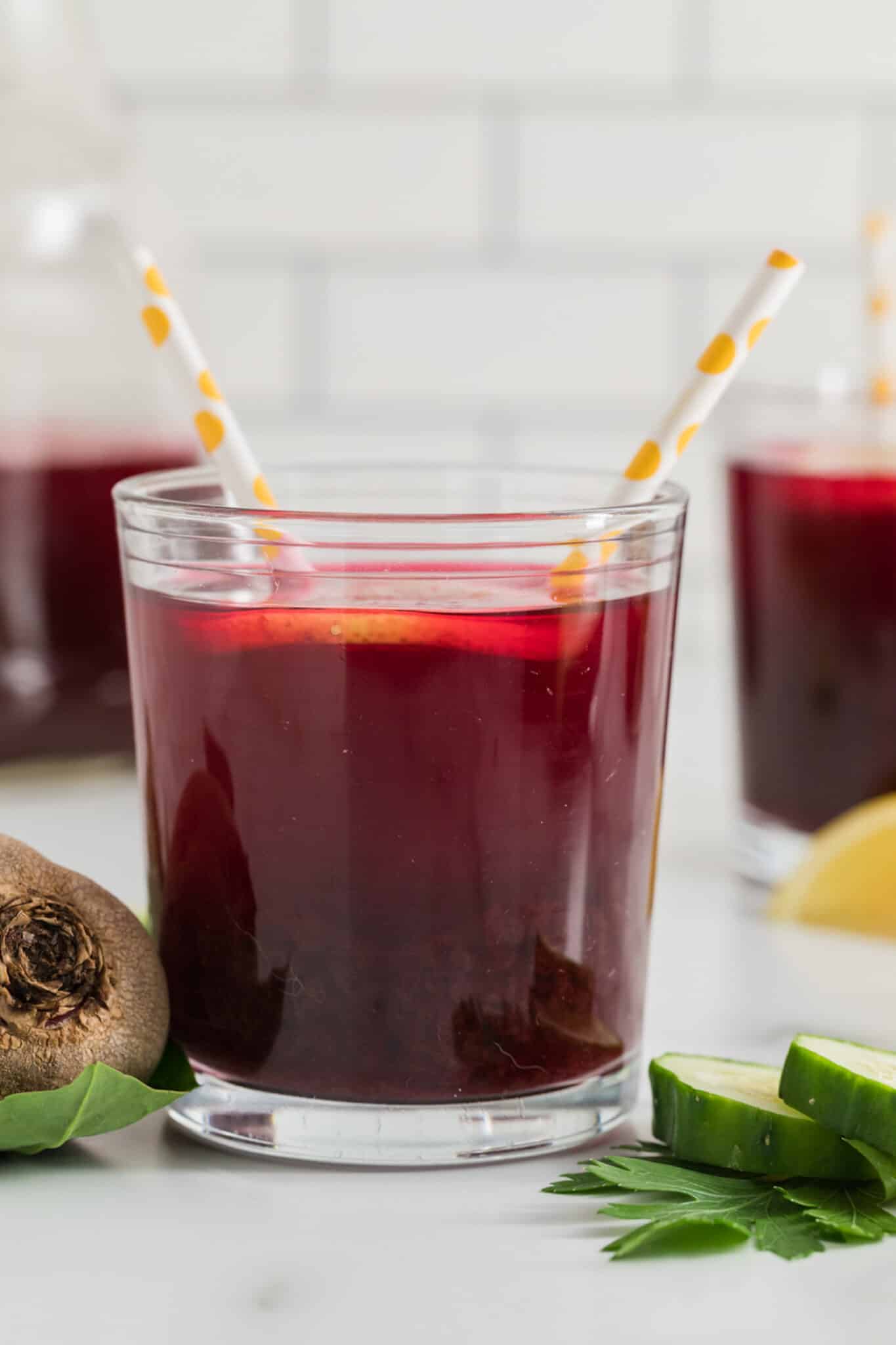 A glass of beet juice with two straws and a lemon slice.