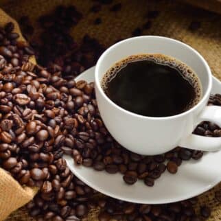 a white mug of coffee surrounded by coffee beans.