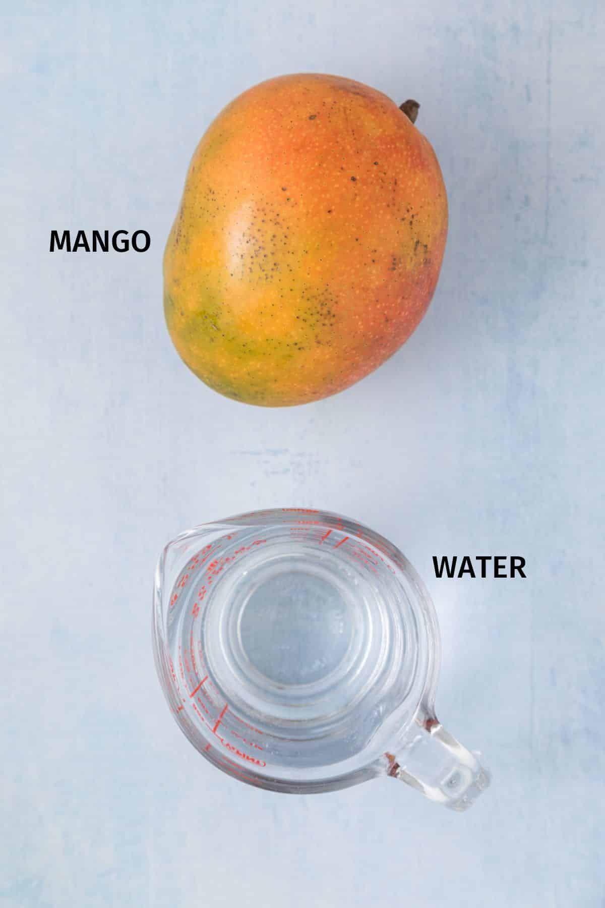 A whole mango and measuring cup of water on a blue surface.