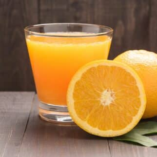 Small glass of orange juice next to two oranges.