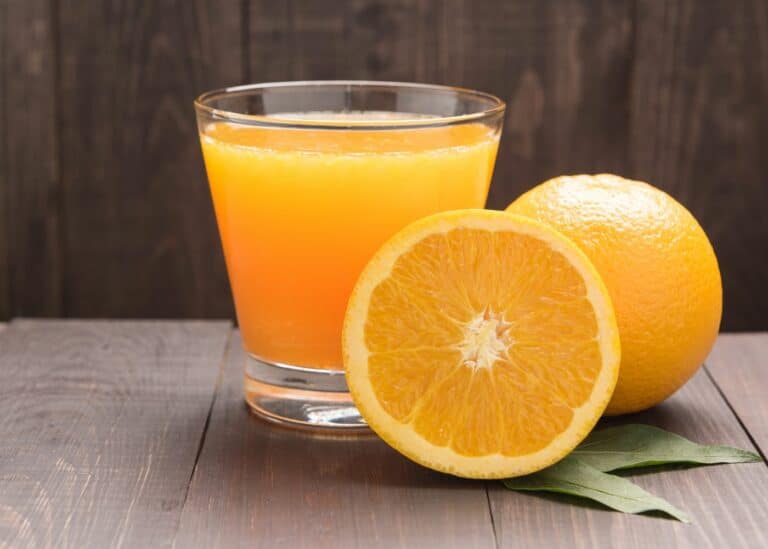 Small glass of orange juice next to two oranges.