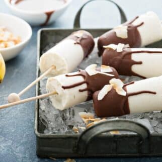 Banana popsicles covered in chocolate sitting in a pan with ice.
