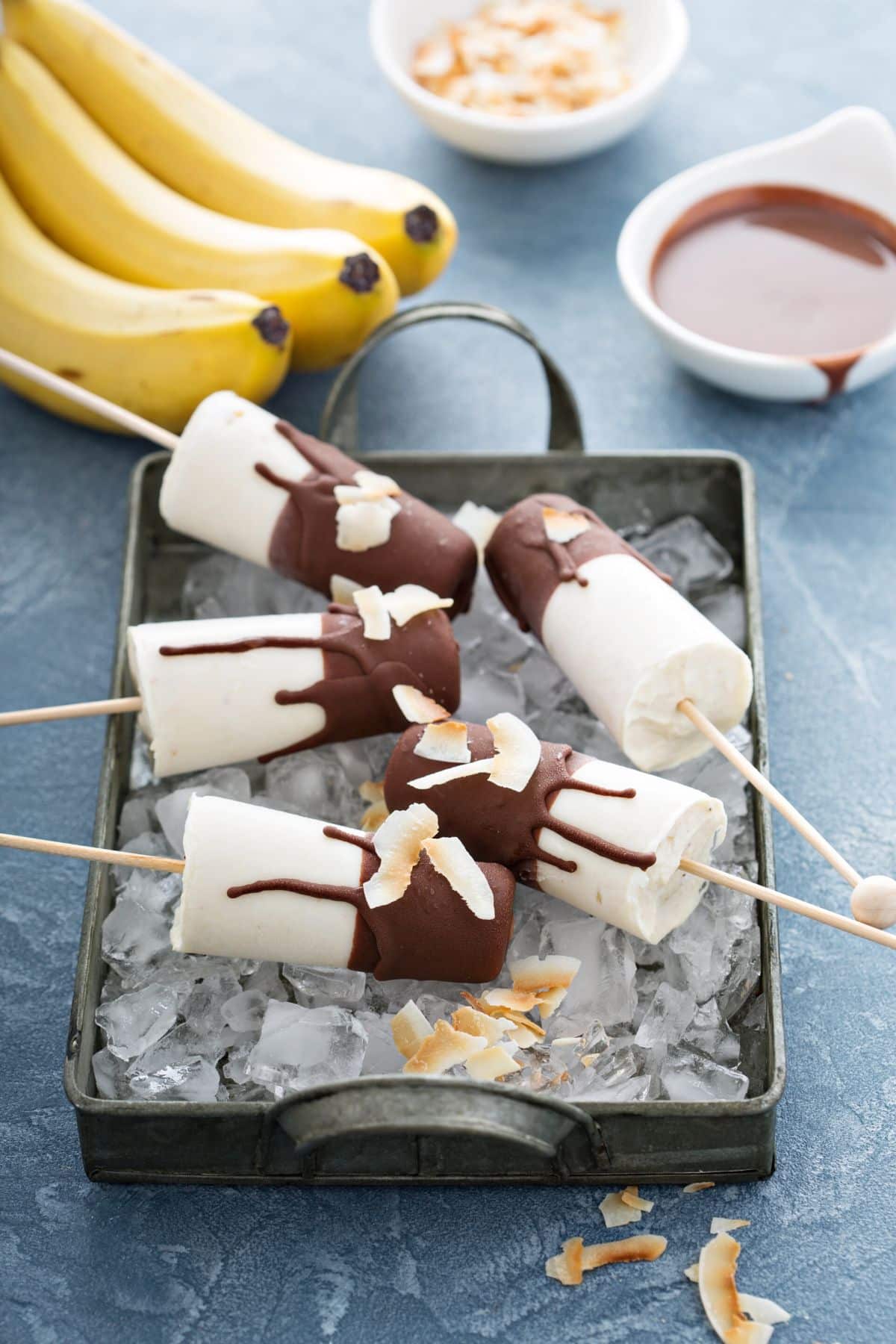 Banana popsicles covered in chocolate sitting in a pan with ice.