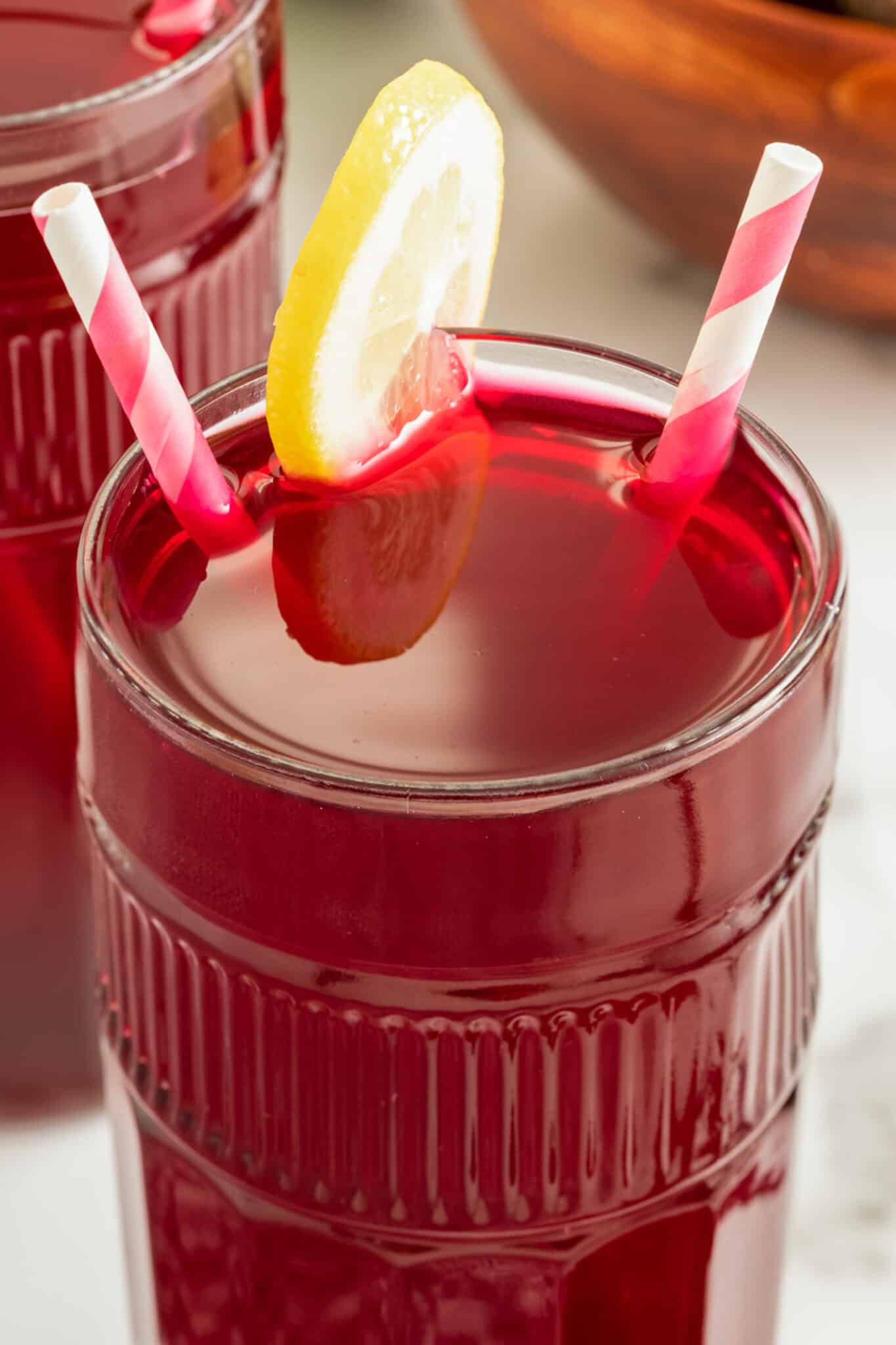 beet juice served in glass with slice of lemon and two striped straws.