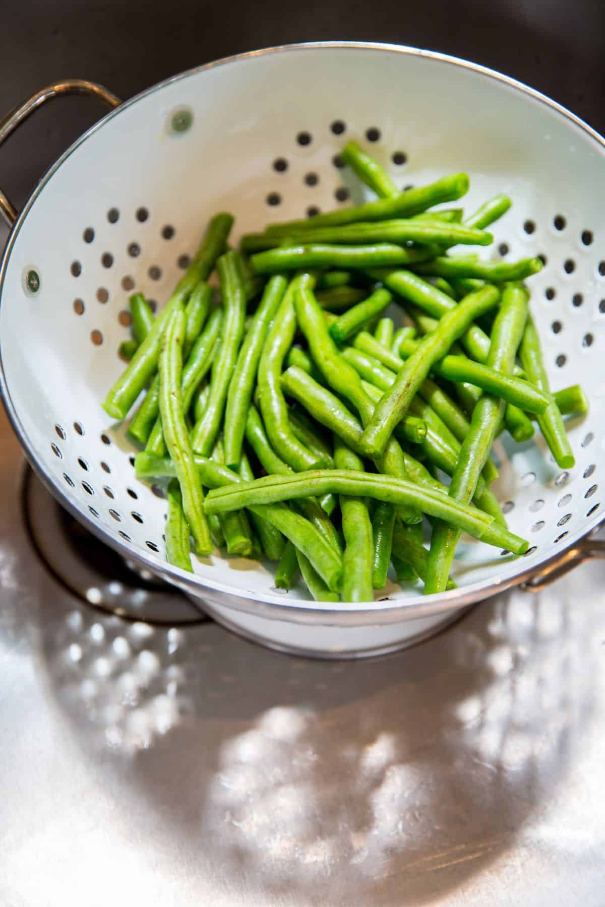 Fresh green beans in a white colander in the sink.