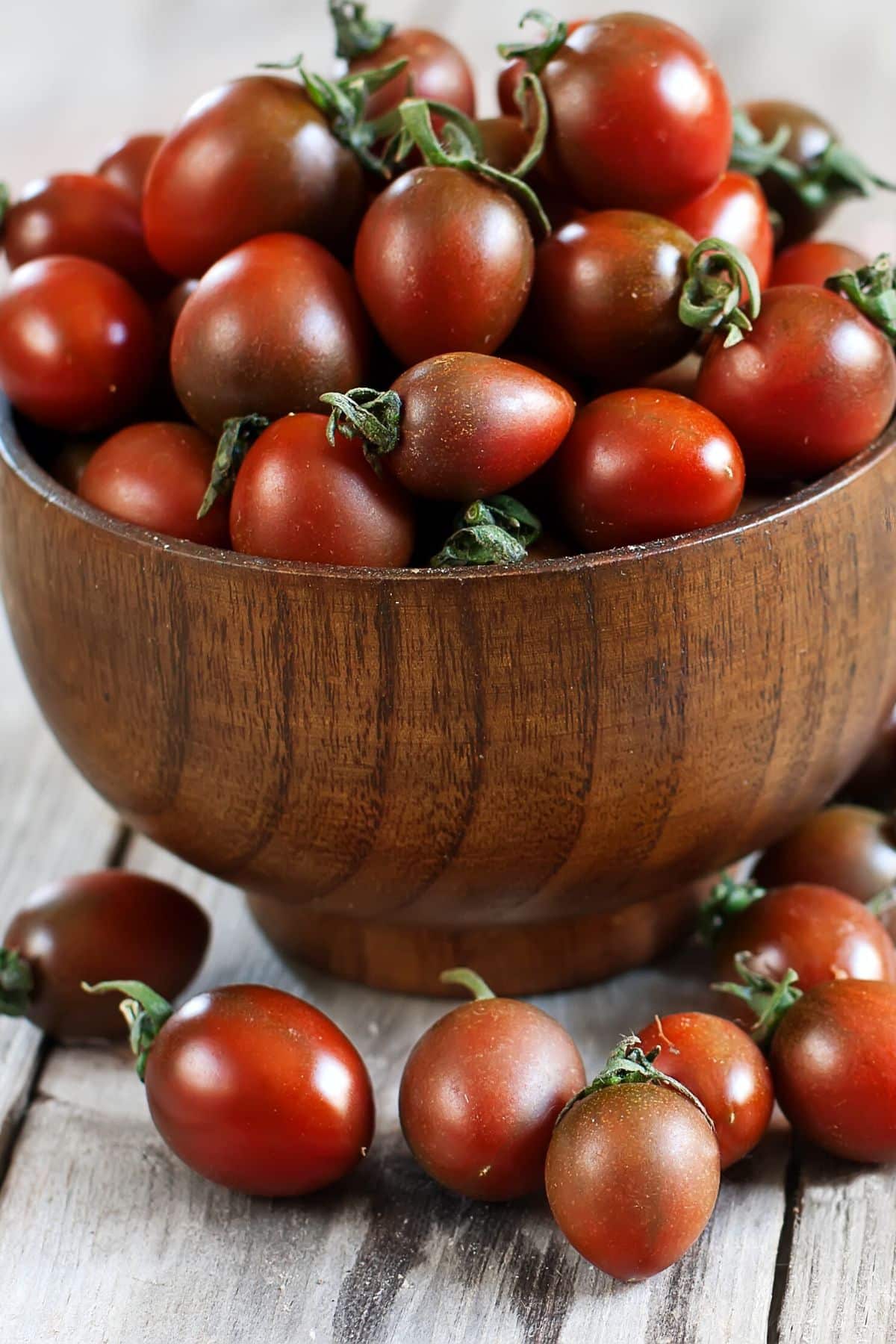 A wooden bowl filled with bright cherry tomatoes.