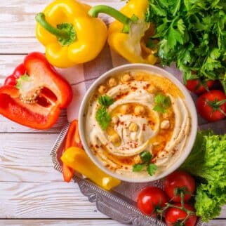A bowl filled with hummus surrounded by tomatoes and peppers.