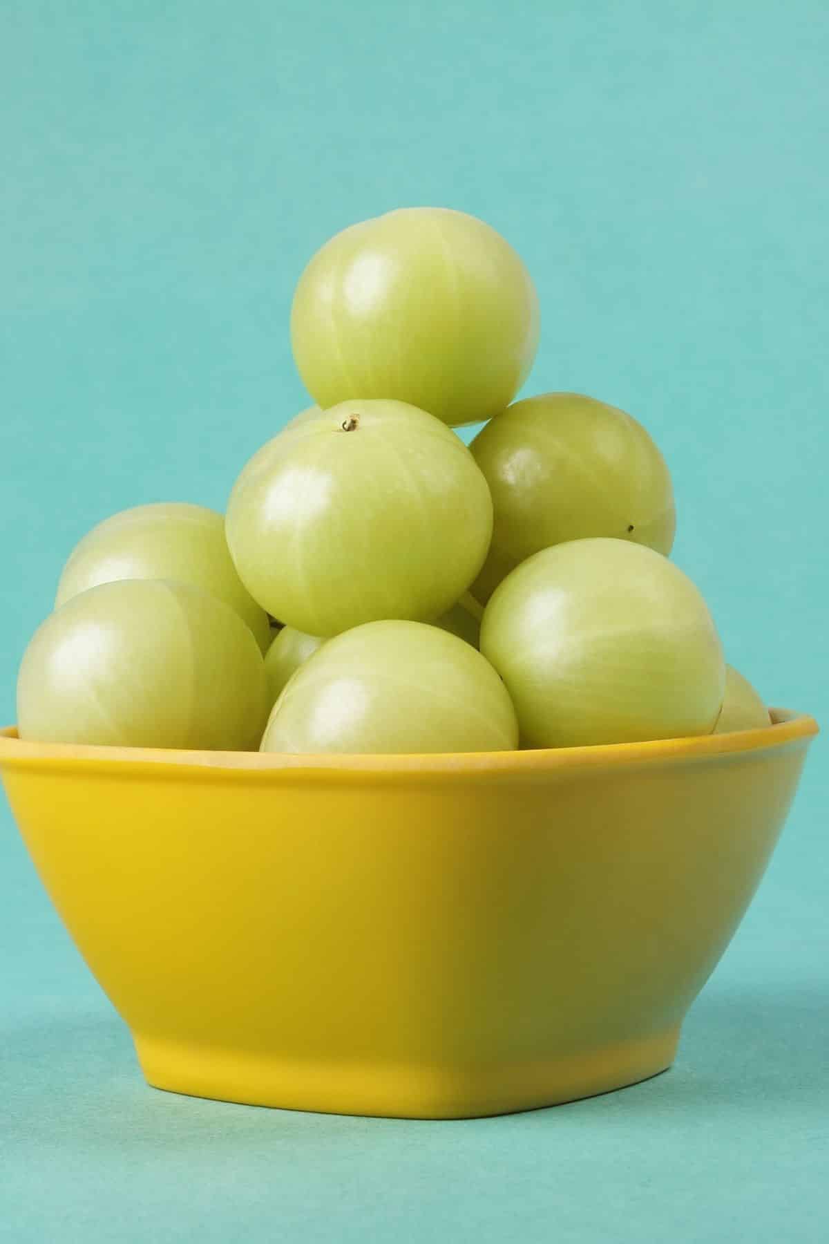 Yellow bowl filled with green indian gooseberries.