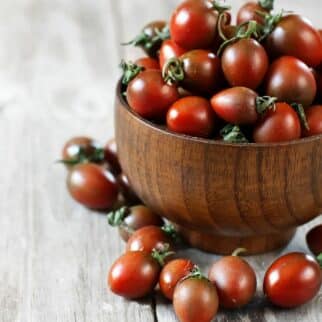 A wooden bowl filled with bright cherry tomatoes.