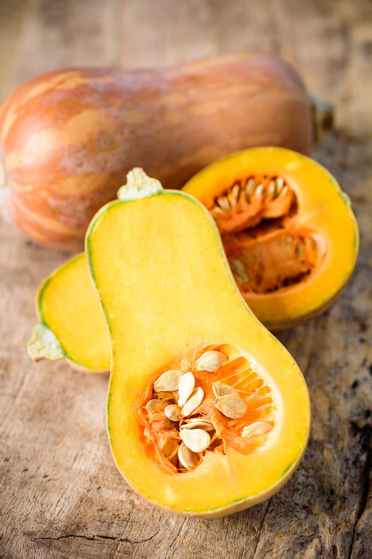 Sliced and whole butternut squash on wooden surface.