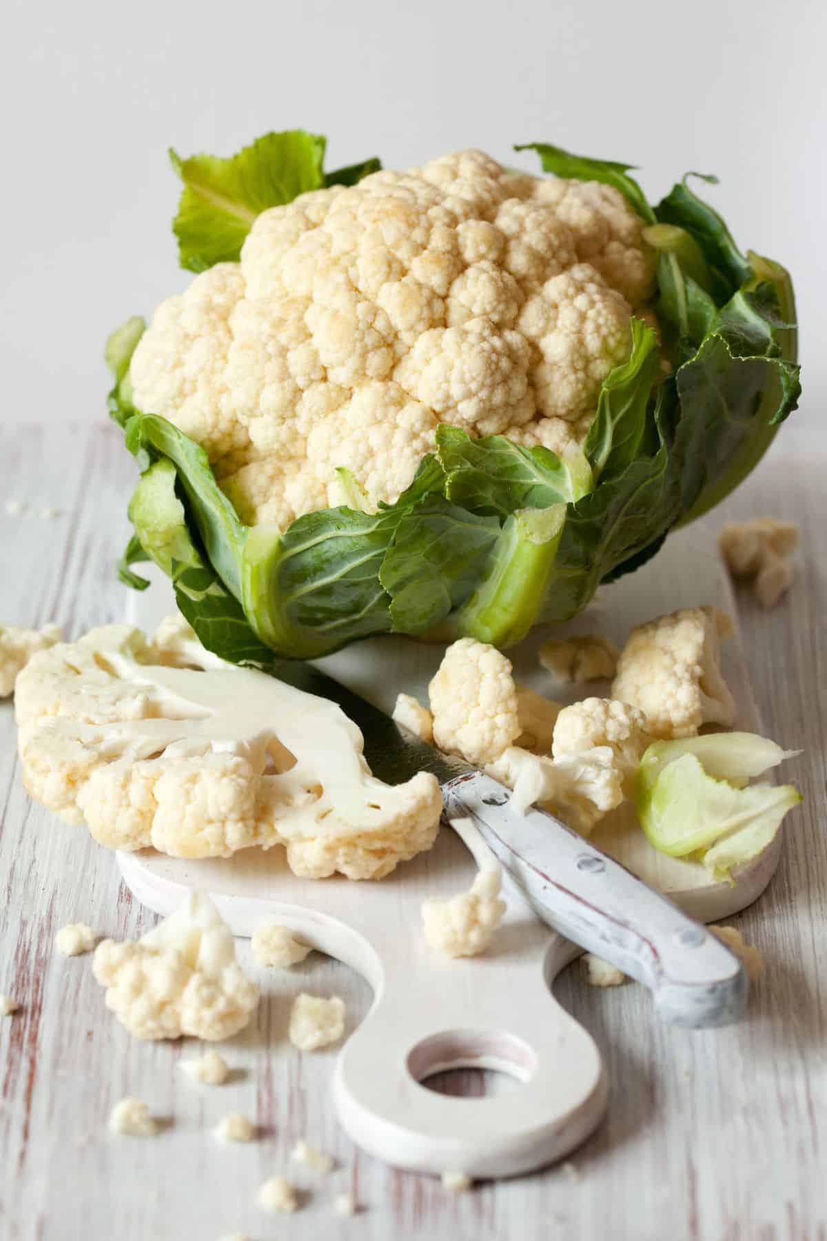 Cauliflower head with cutting board and sliced cauliflower.