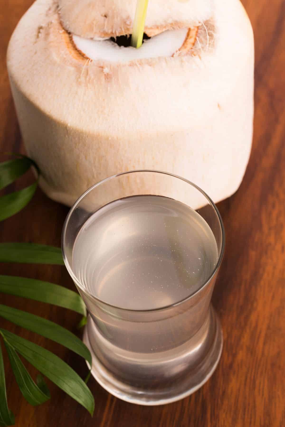 A small glass of coconut water in front of a chunk of coconut.
