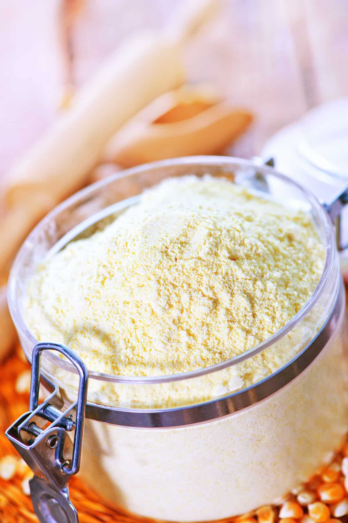 Container of corn flour with corn kernels on table.