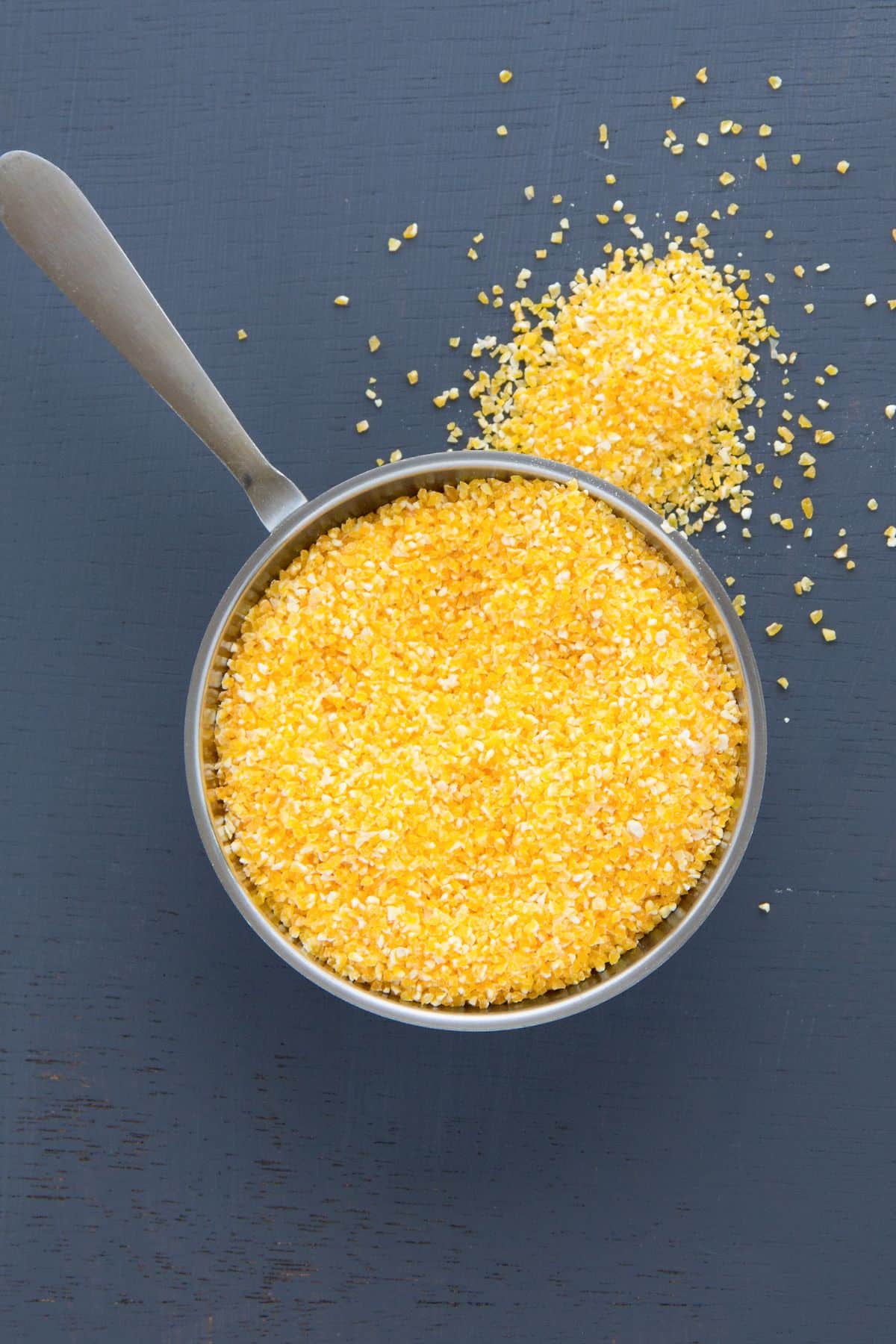 Uncooked corn grits in pan on dark surface.