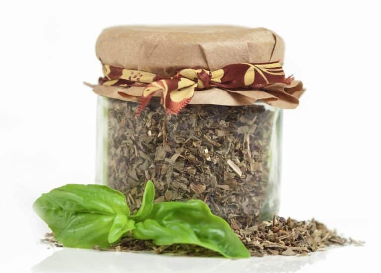 Glass jar filled with dry basil with a paper top.