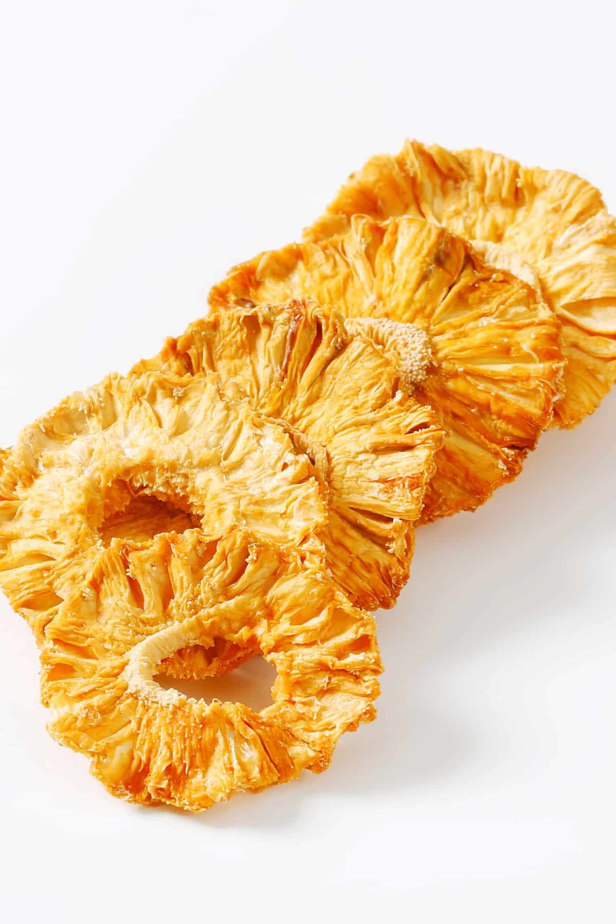 A row of dehydrated pineapple rings on a white surface.