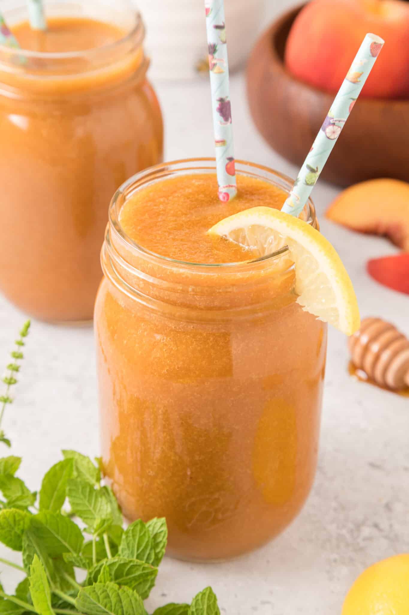 A jar of peach juice with two straws and a lemon slice.