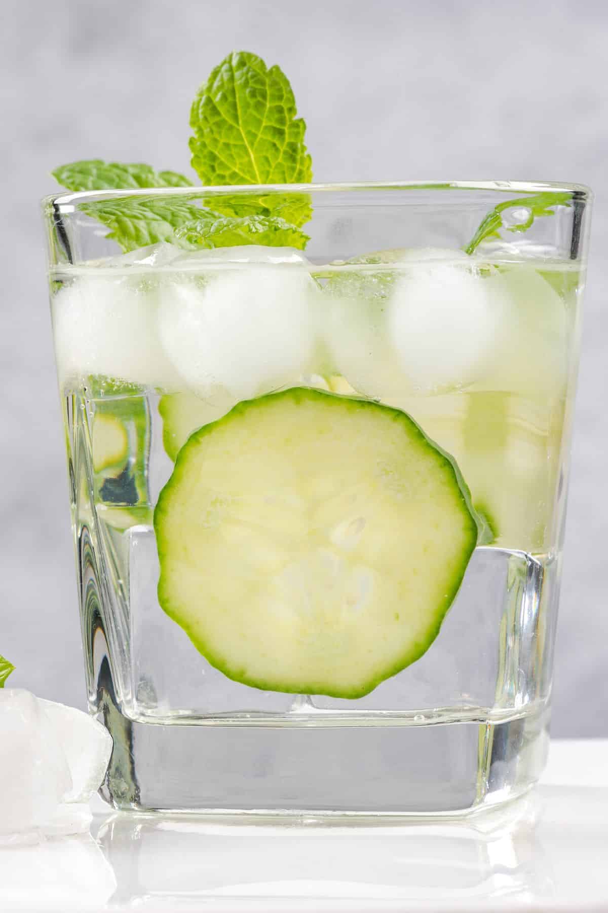 A glass of water with fresh cucumber slices and ice cubes.
