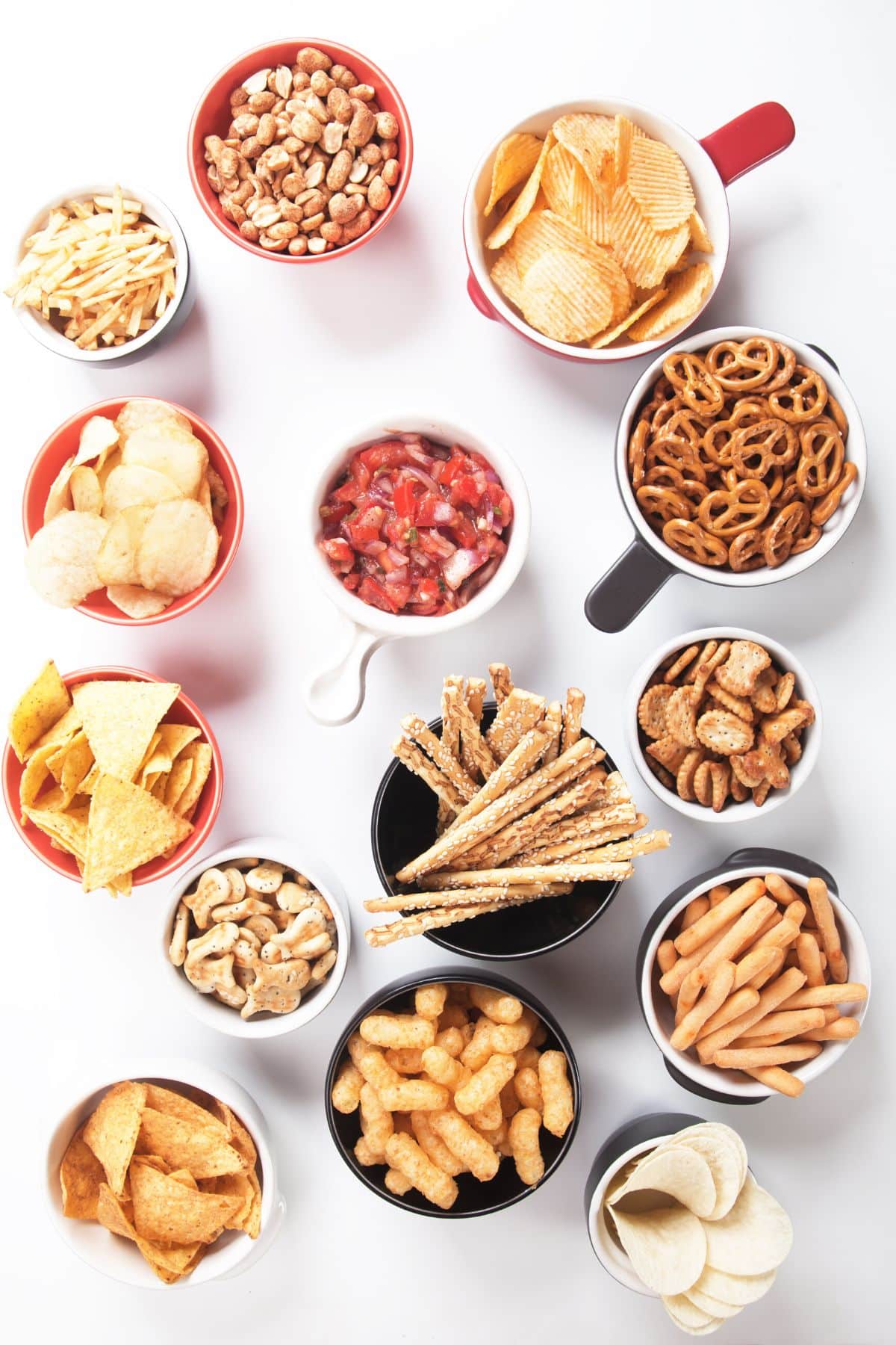 Various snacks in small cups and bowls on a white surface.